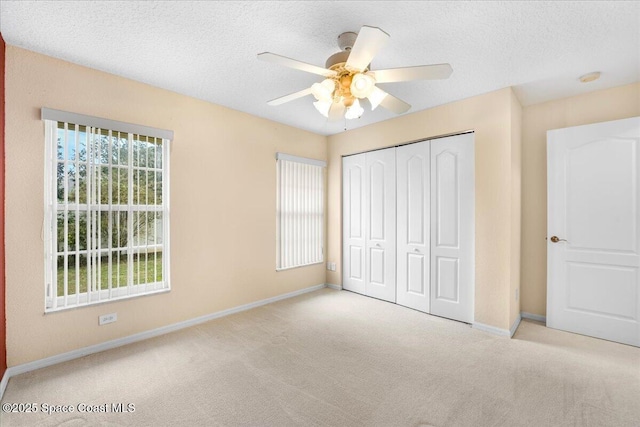 unfurnished bedroom featuring a textured ceiling, a closet, light carpet, and baseboards