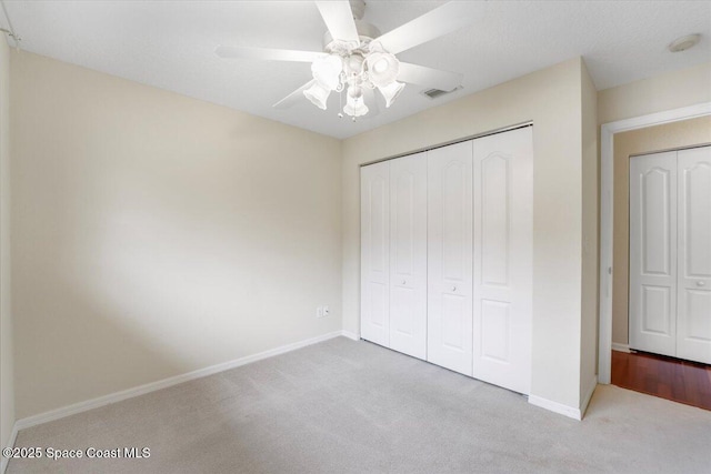 unfurnished bedroom featuring ceiling fan, light carpet, visible vents, baseboards, and a closet