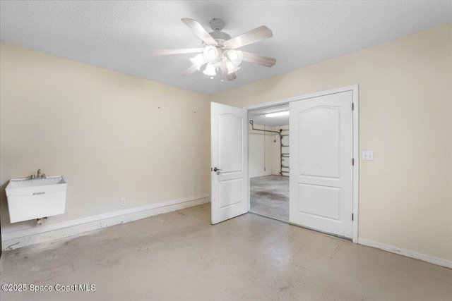 unfurnished bedroom with finished concrete flooring, baseboards, a ceiling fan, a textured ceiling, and a sink