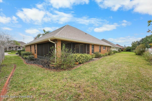 view of side of property featuring a sunroom, roof with shingles, and a yard