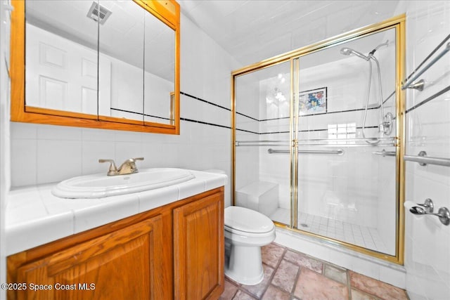 bathroom with stone tile floors, visible vents, toilet, a shower stall, and vanity