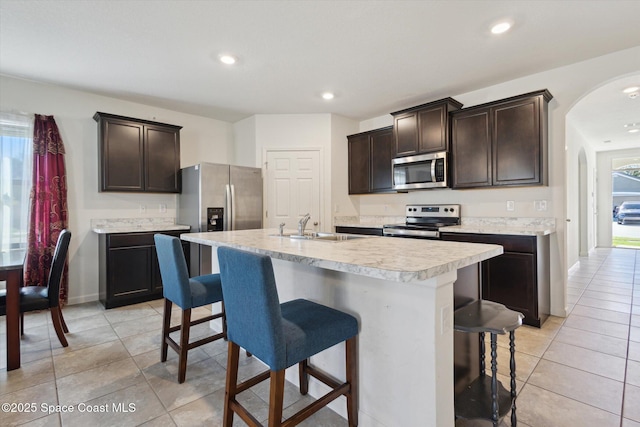 kitchen with a kitchen island with sink, stainless steel appliances, a sink, light countertops, and a kitchen bar