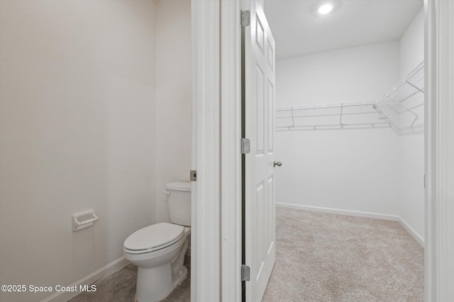 bathroom with toilet, a spacious closet, and baseboards