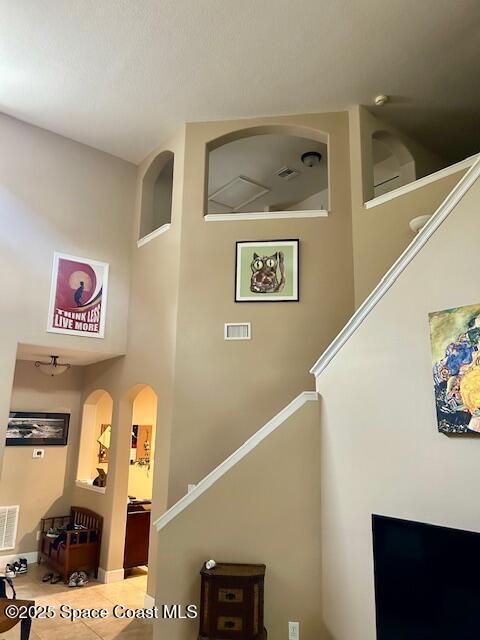 stairs featuring arched walkways, a high ceiling, tile patterned flooring, and visible vents