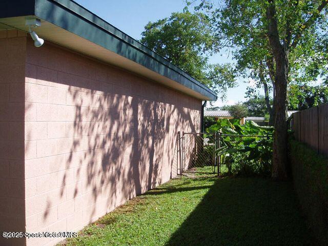 view of property exterior featuring concrete block siding, fence, and a lawn