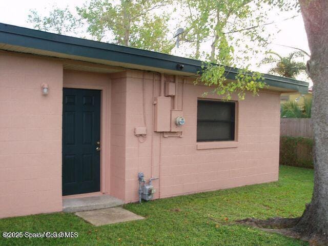 property entrance with a yard, concrete block siding, and fence