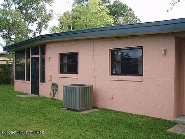 view of side of property featuring a sunroom, a lawn, and central AC