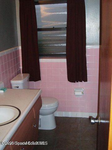 bathroom featuring toilet, wainscoting, tile walls, and vanity