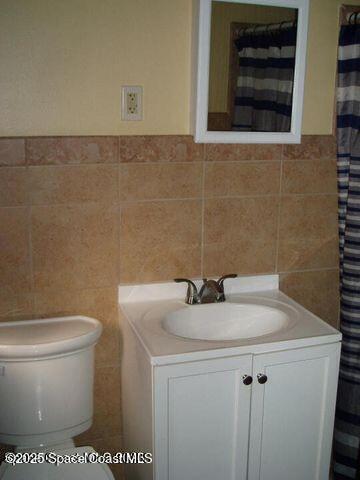 full bath with toilet, tile walls, and vanity