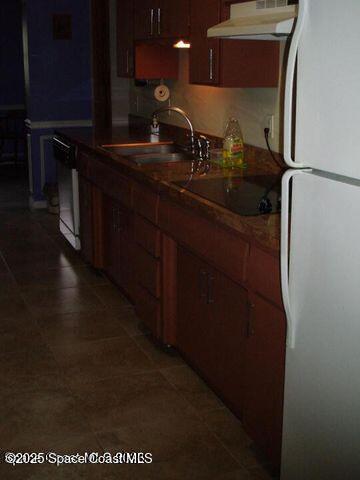 kitchen with freestanding refrigerator, a sink, under cabinet range hood, dishwashing machine, and black electric cooktop