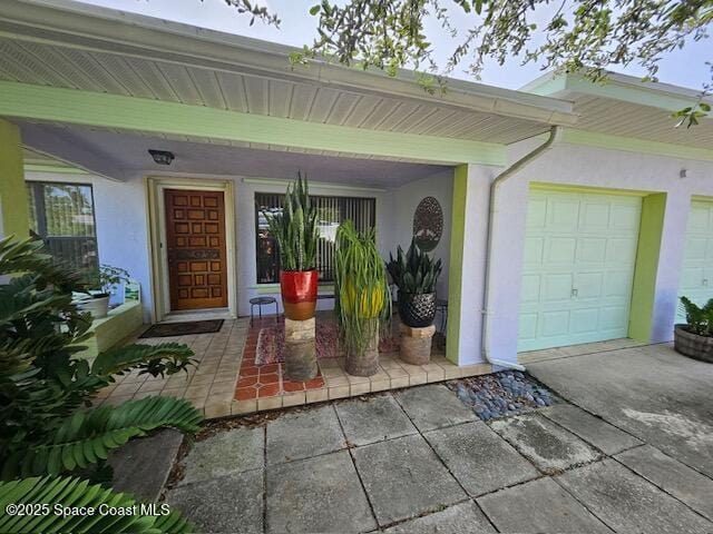 view of exterior entry featuring an attached garage, driveway, a porch, and stucco siding