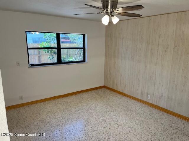 124 E Dover St E, Satellite Beach, FL 32937 - unfurnished room featuring baseboards, speckle patterned floor, a ceiling fan, and wooden walls