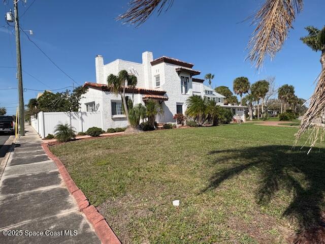 view of side of property with stucco siding, a chimney, fence, and a yard