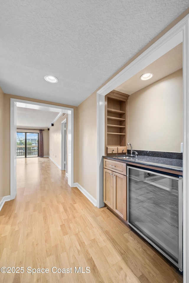 kitchen featuring beverage cooler, dark countertops, a textured ceiling, light wood-style floors, and a sink