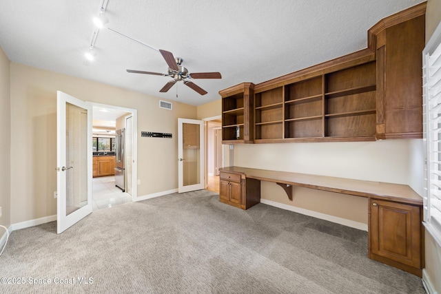 unfurnished office with baseboards, built in study area, visible vents, and light colored carpet