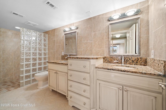 bathroom featuring tile patterned flooring, toilet, visible vents, tile walls, and walk in shower