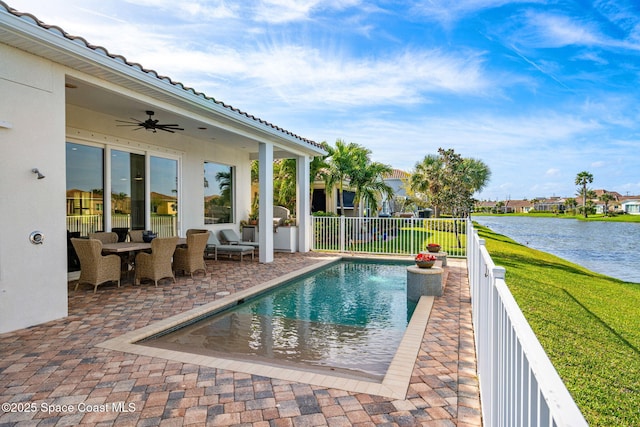 view of swimming pool featuring a ceiling fan, fence, a water view, a patio area, and a lawn