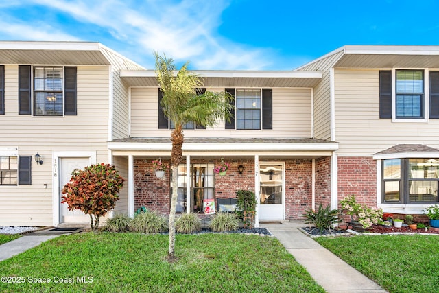 multi unit property with brick siding, a front lawn, and a porch