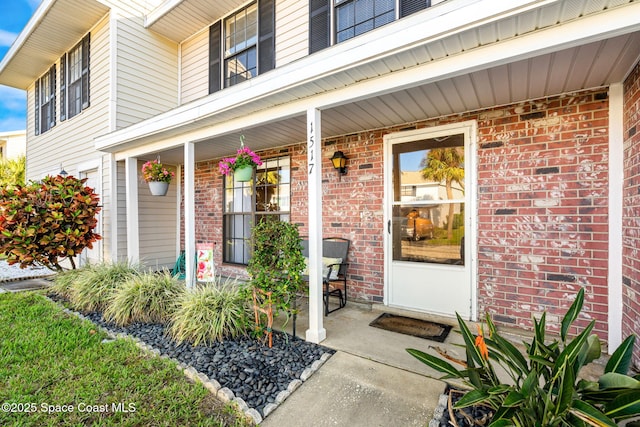 view of exterior entry featuring covered porch and brick siding