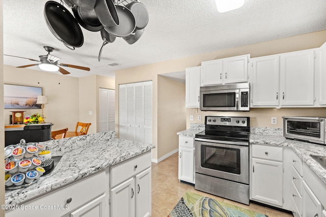 kitchen with a toaster, appliances with stainless steel finishes, white cabinets, a textured ceiling, and light stone countertops