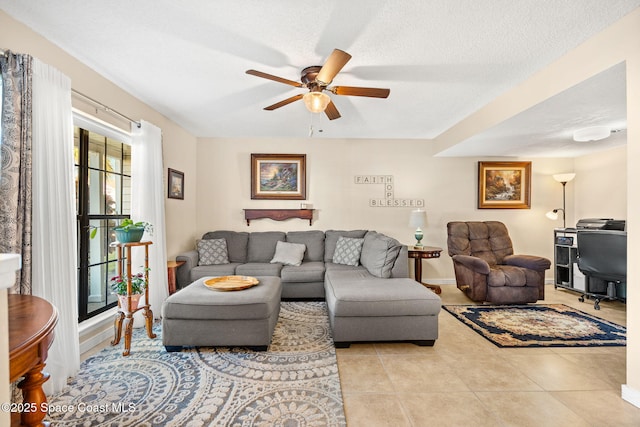 living area featuring a ceiling fan, light tile patterned flooring, a textured ceiling, and baseboards