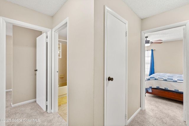 hall featuring light carpet, a textured ceiling, and baseboards