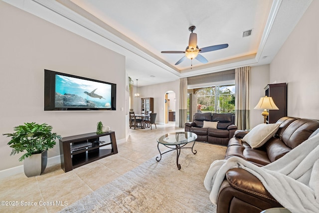 living room with arched walkways, light tile patterned floors, a raised ceiling, visible vents, and baseboards