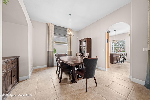 dining space featuring arched walkways, light tile patterned floors, and baseboards