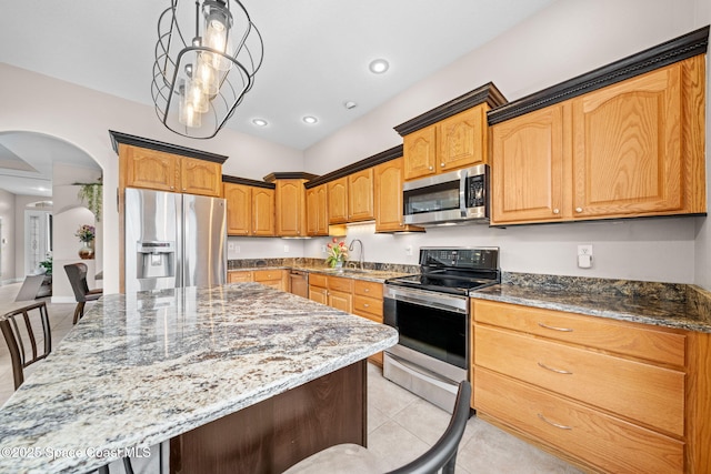 kitchen with light tile patterned floors, stainless steel appliances, a kitchen island, a sink, and dark stone countertops