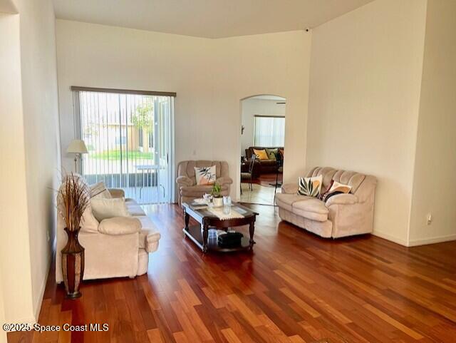 living area with arched walkways, baseboards, and wood finished floors