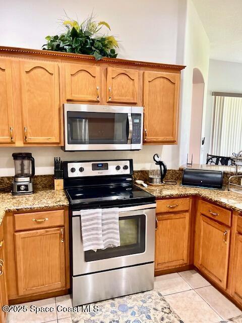 1401 Rila St SE, Palm Bay, FL 32909 - kitchen with stainless steel appliances, light tile patterned flooring, a peninsula, light stone countertops, and brown cabinetry
