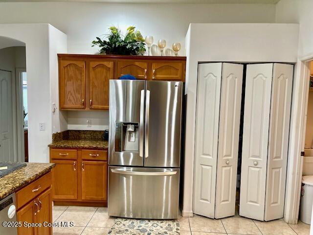 1401 Rila St SE, Palm Bay, FL 32909 - kitchen featuring brown cabinets, light tile patterned floors, stainless steel appliances, arched walkways, and dark stone counters