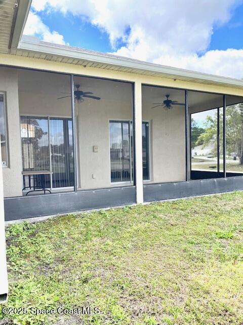 1401 Rila St SE, Palm Bay, FL 32909 - rear view of property featuring a ceiling fan, a sunroom, stucco siding, and a lawn