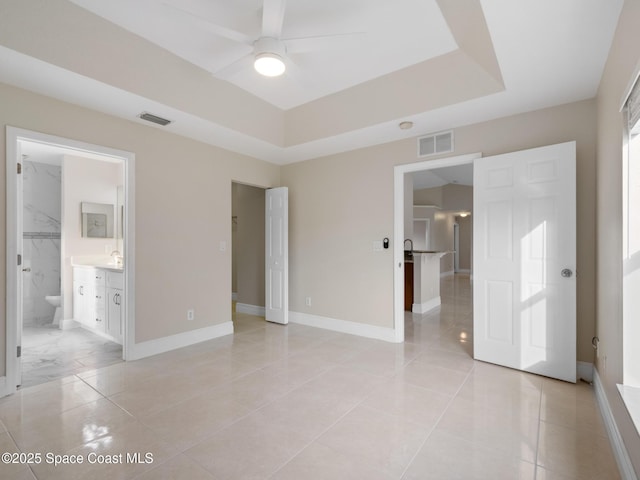 unfurnished bedroom with a tray ceiling, a sink, visible vents, and baseboards