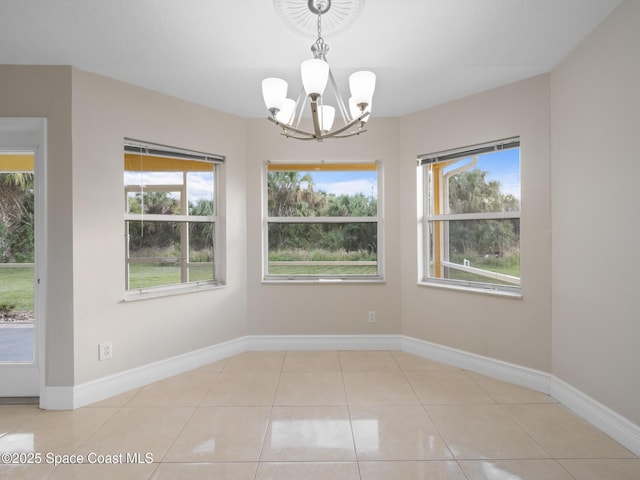 unfurnished dining area featuring a chandelier, plenty of natural light, tile patterned flooring, and baseboards