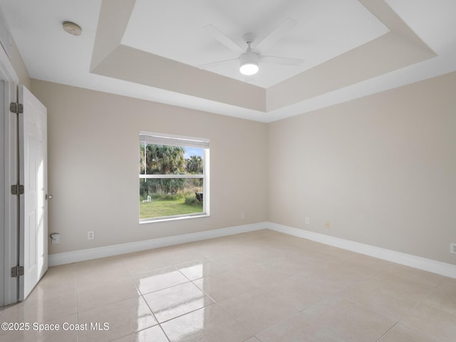 unfurnished room featuring ceiling fan, light tile patterned flooring, a raised ceiling, and baseboards