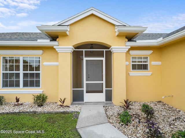 doorway to property with a shingled roof and stucco siding