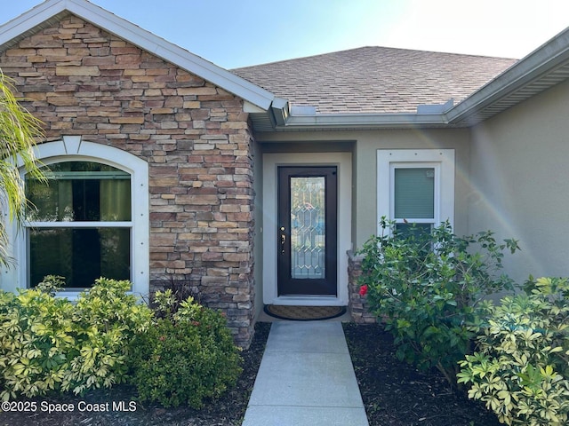 entrance to property with stone siding, roof with shingles, and stucco siding