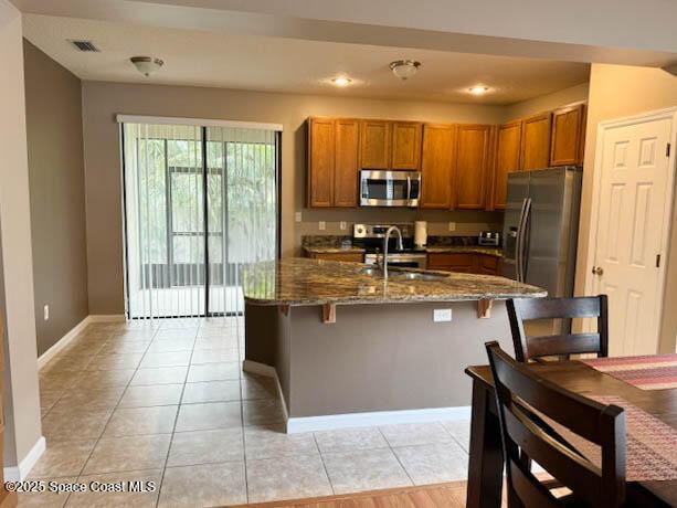 kitchen featuring visible vents, appliances with stainless steel finishes, light tile patterned flooring, brown cabinetry, and a sink