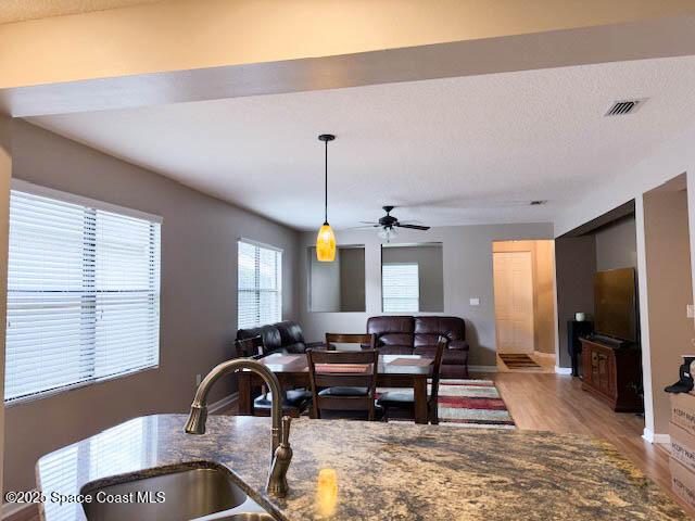 living area with visible vents, baseboards, light wood-type flooring, a textured ceiling, and a ceiling fan