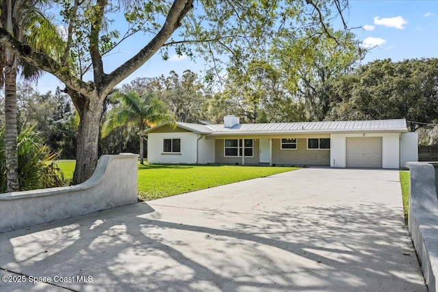 single story home with metal roof, an attached garage, brick siding, concrete driveway, and a front yard