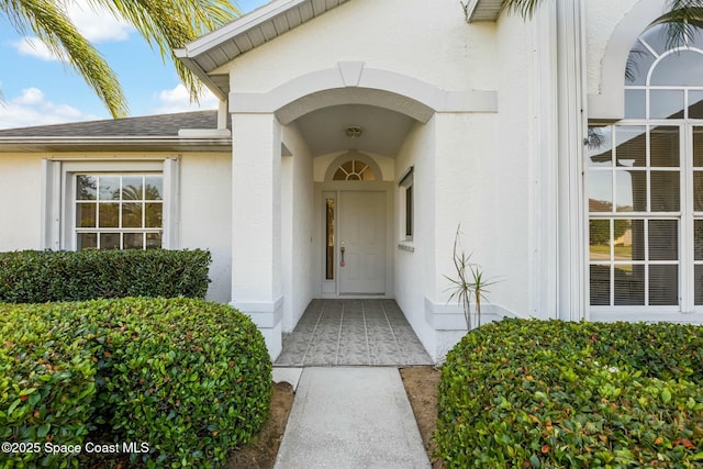 property entrance featuring a shingled roof and stucco siding