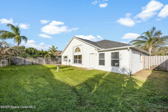 rear view of property with roof with shingles, a fenced backyard, a lawn, and stucco siding