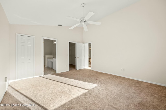 unfurnished bedroom featuring a walk in closet, light colored carpet, visible vents, ensuite bathroom, and high vaulted ceiling