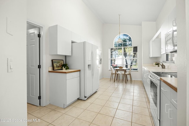 kitchen featuring light tile patterned floors, white appliances, a sink, white cabinetry, and hanging light fixtures