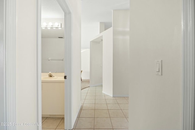 corridor featuring light tile patterned floors, a sink, and baseboards