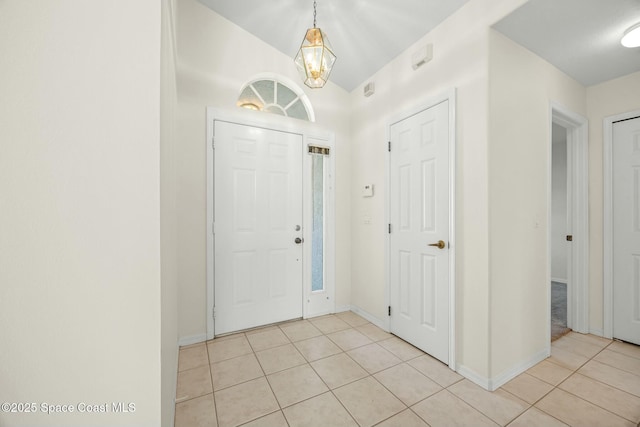 foyer featuring lofted ceiling, baseboards, an inviting chandelier, and light tile patterned floors