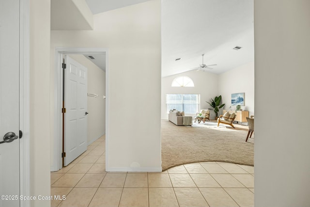 hall with lofted ceiling, light colored carpet, visible vents, and light tile patterned floors