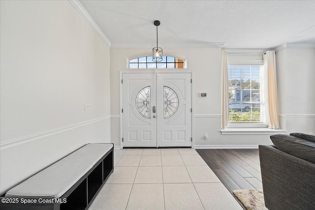 foyer entrance with light wood-style floors, baseboards, ornamental molding, and a textured ceiling