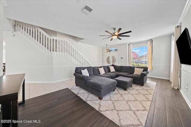 living room with light wood-style floors, visible vents, a textured ceiling, and stairs